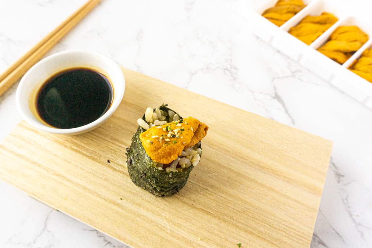 A piece of nigiri on a wooden sushi board with soy sauce.