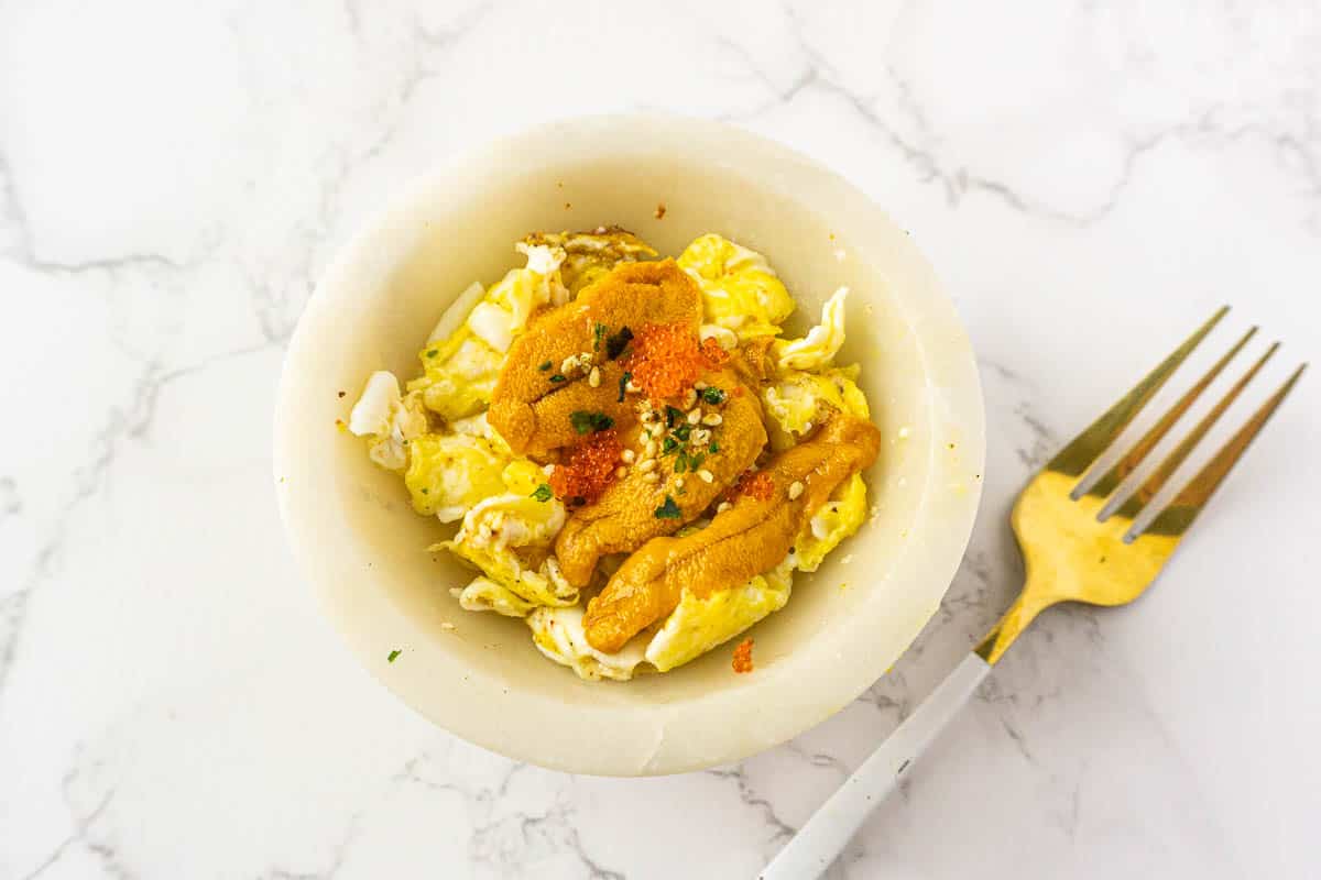 Uni scrambled eggs in a small white bowl with a fork on the side.