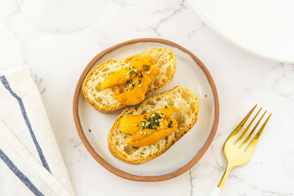 Two pieces of uni toast on a plate with a fork and linen on the side.