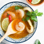 Wooden spoon picking up a shrimp in a bowl of Tom Yum.