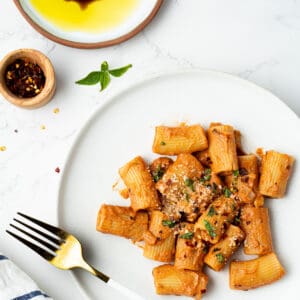 Spicy rigatoni with red pepper flakes and olive oil plate on the side.