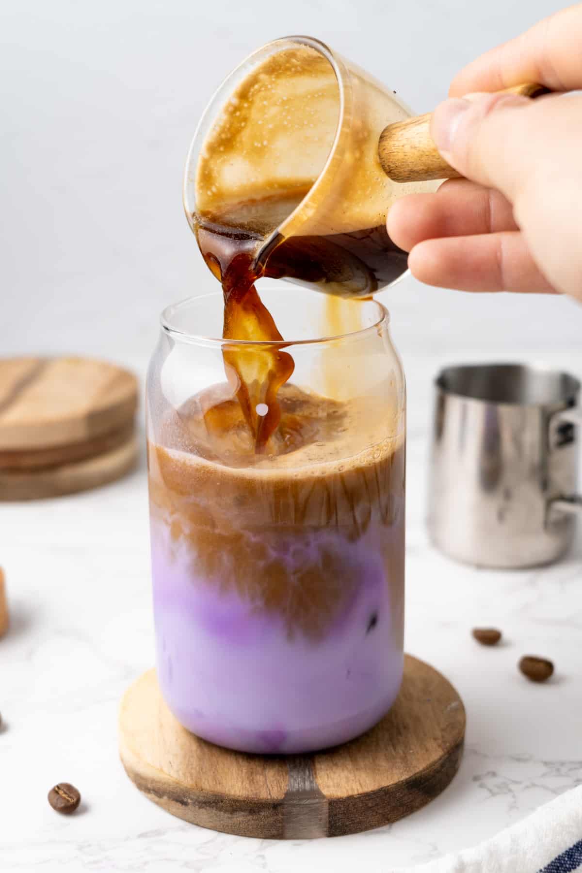 Pouring a shot of espresso into a glass of ube latte.
