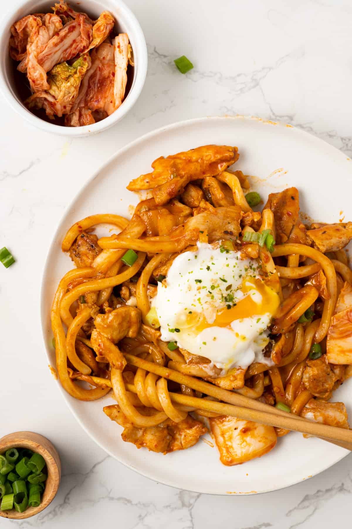 Kimchi udon with a poached egg with chopsticks twirling the noodles.