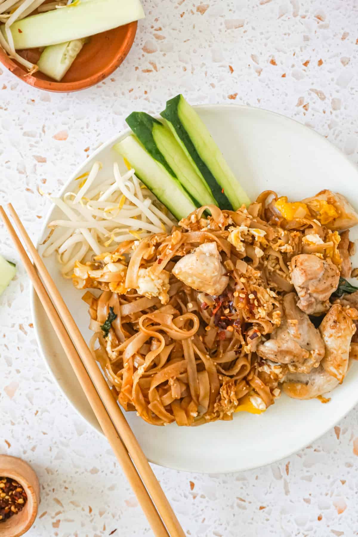 A plate of chicken pad see ew with a side of chopsticks. 