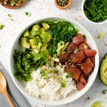 A overhead shot of a tuna poke bowl surrounded by toppings.