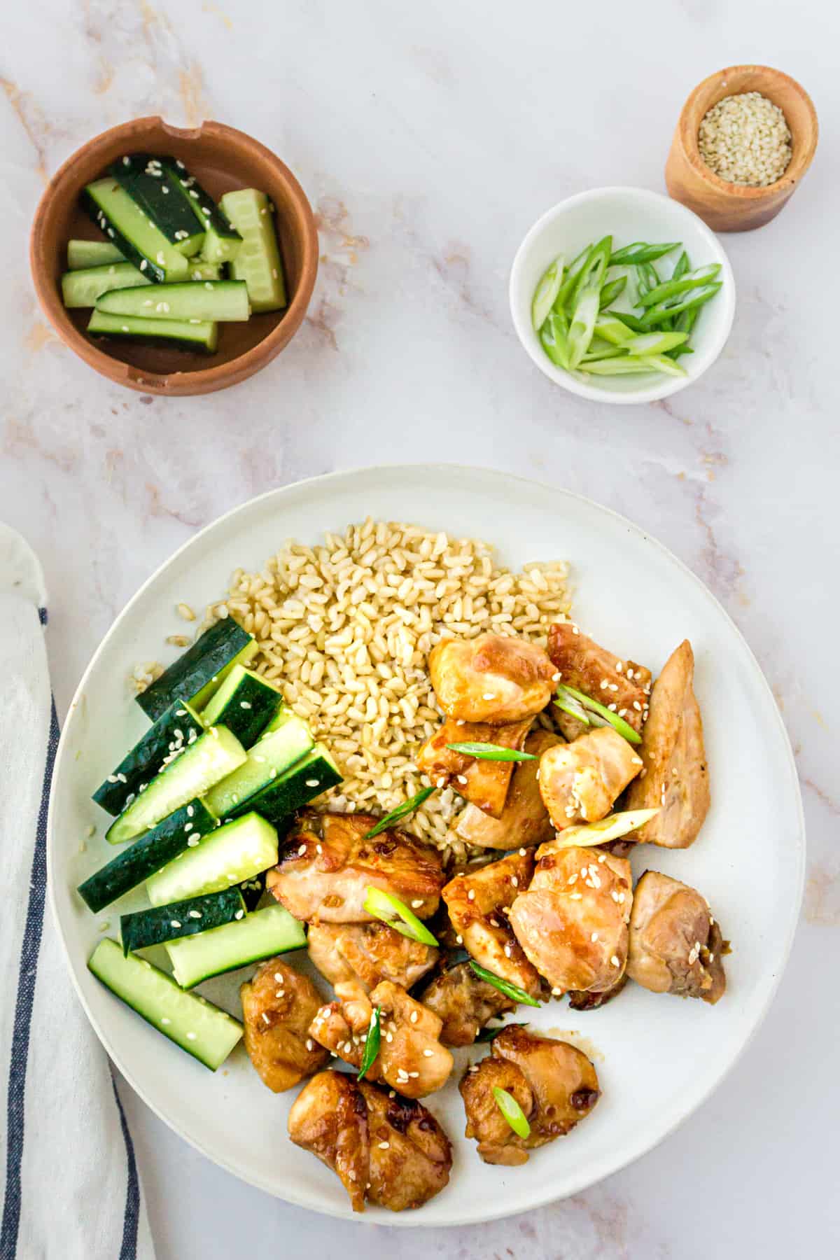 A plate of teriyaki chicken with cucumbers and scallions.