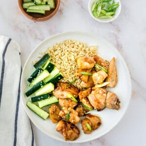 A plate of teriyaki chicken with cucumbers and scallions.
