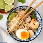 Bowl of tom yum noodles with chopsticks twirled around the noodles.