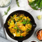 Overhead shot of cha ca in a cast iron, served with herbs and rice noodles.
